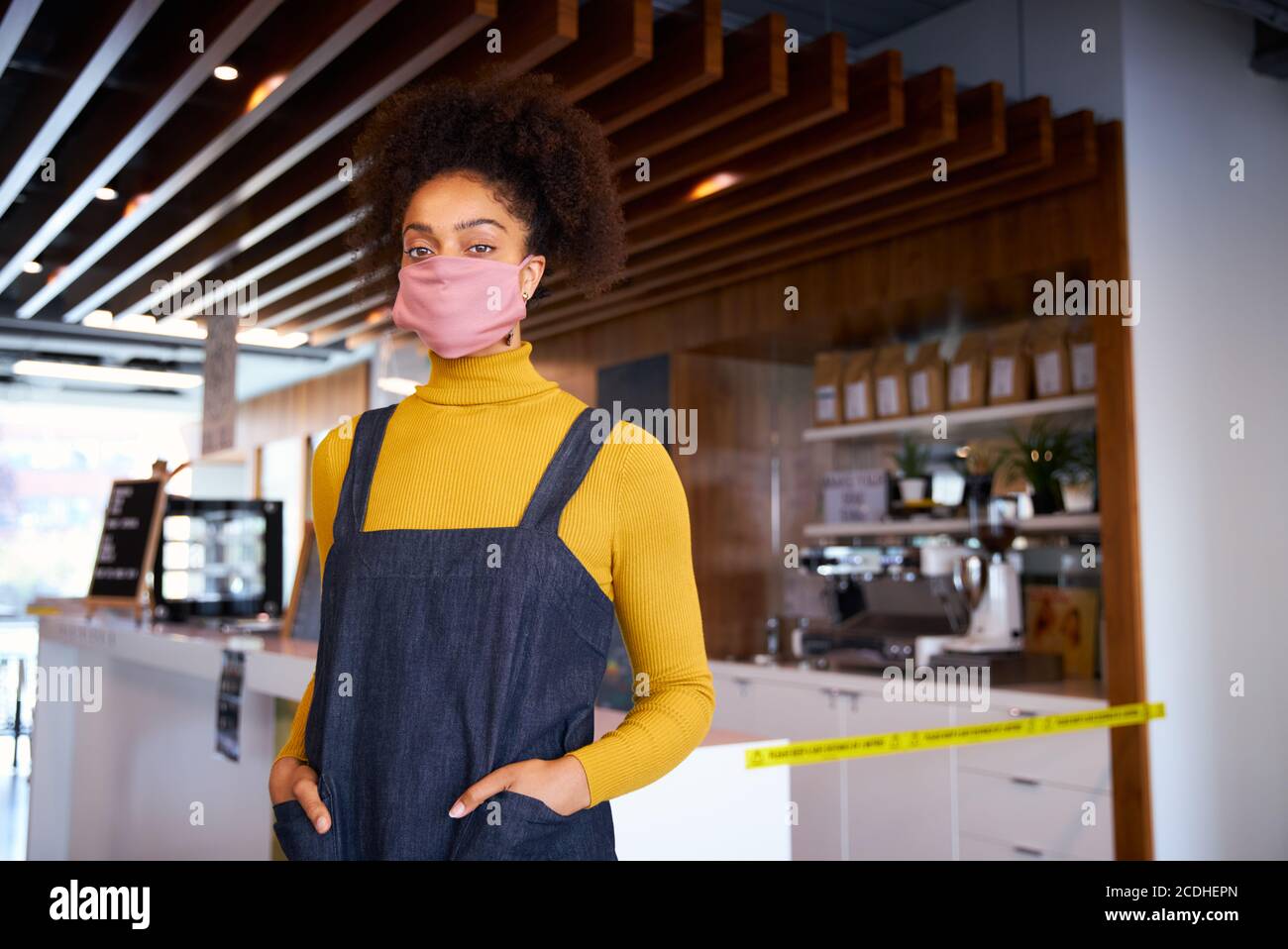 Donna African coffee shop proprietario indossare maschera viso in piedi parte anteriore del contatore Foto Stock