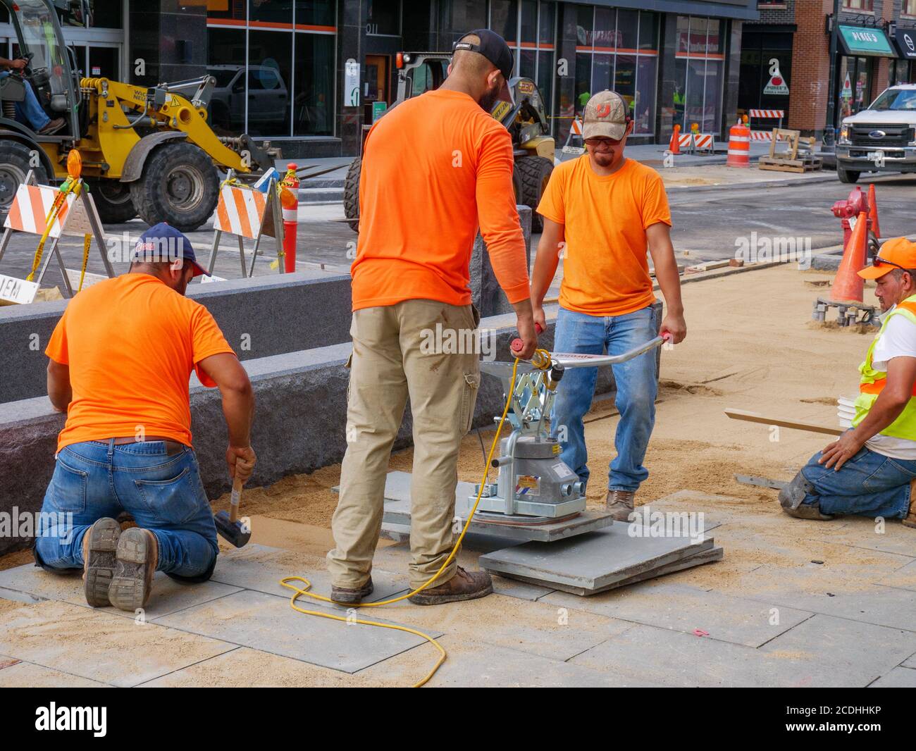 Lavoratori edili che utilizzano un sollevatore elettrico a ventosa per posizionare i blocchi di pavimentazione sul progetto di ricostruzione Lake Street. Oak Park, Illinois. Foto Stock