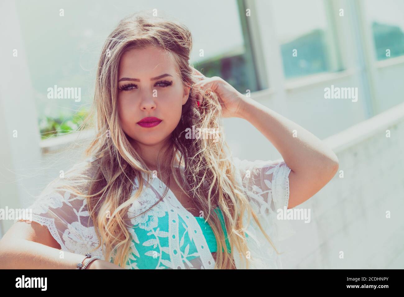 Bella giovane ragazza bionda con capelli lunghi che soffiano nel vento all'aperto. Occhi blu. In riva al mare, colori chiari e luminosi. Giorno con sole intenso. Foto Stock