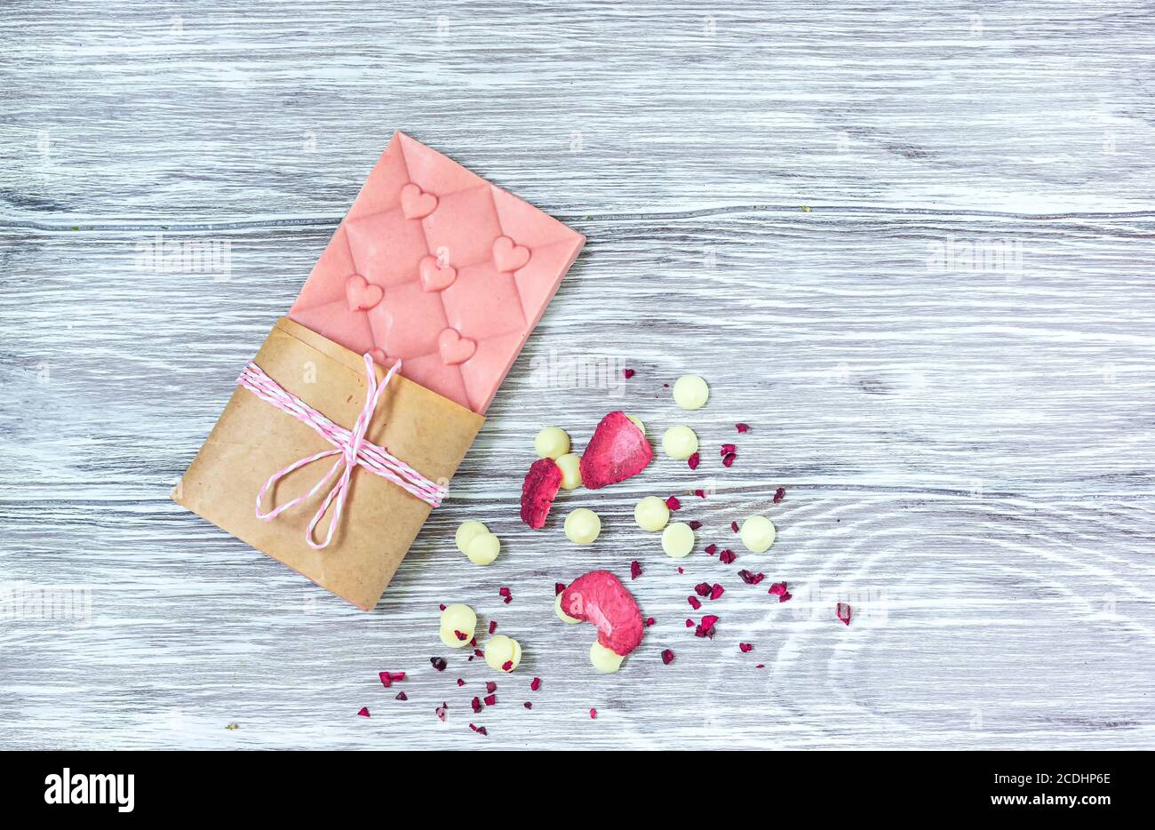 Barretta di cioccolato rosa decorata con fette di frutta a guscio e fette su sfondo grigio. Cioccolato artigianale alla moda. Idea regalo. Foto Stock