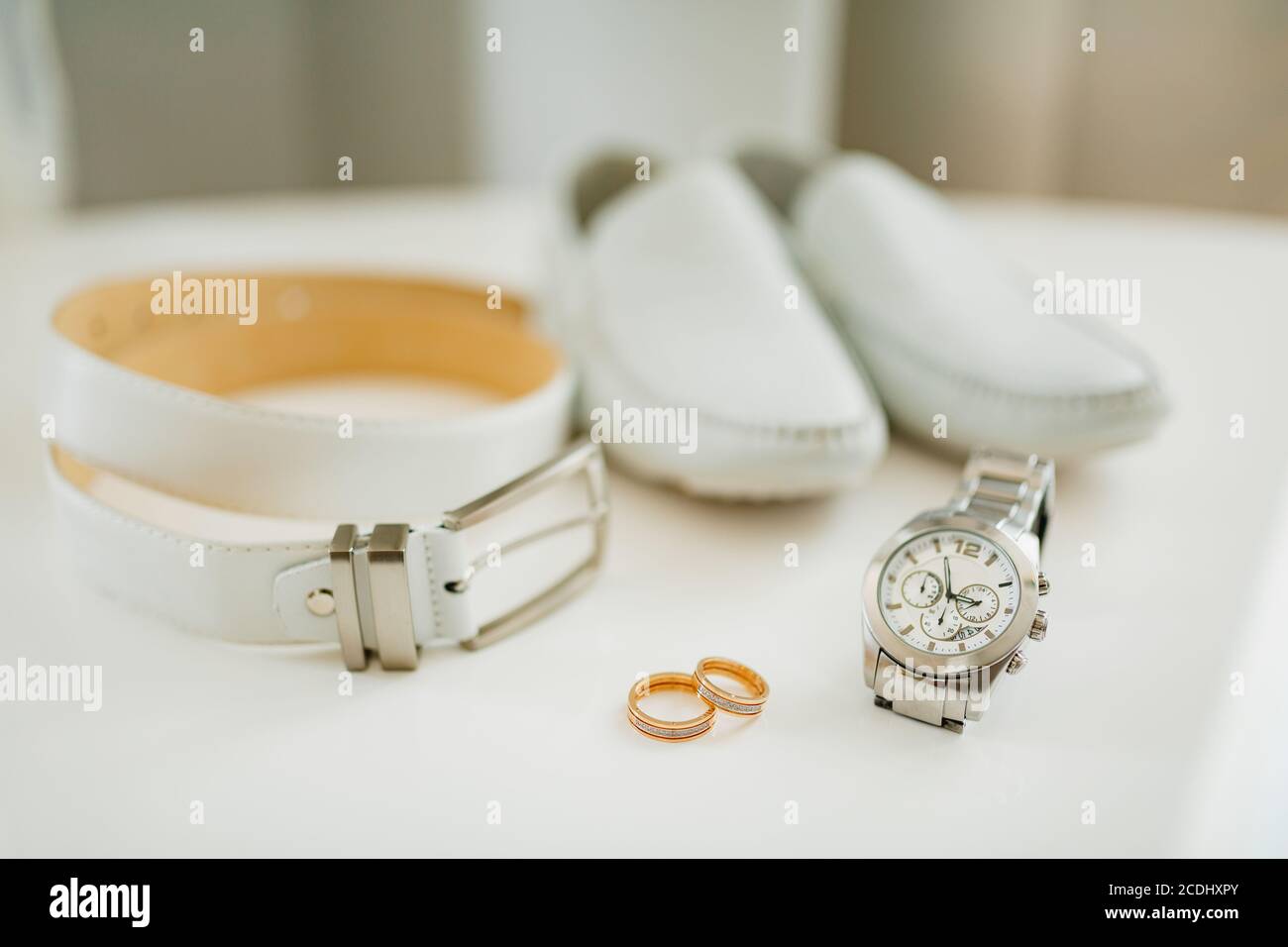 Due anelli da sposa con accessori per lo sposo. Orologio da polso, cintura  in pelle e scarpe su sfondo bianco Foto stock - Alamy