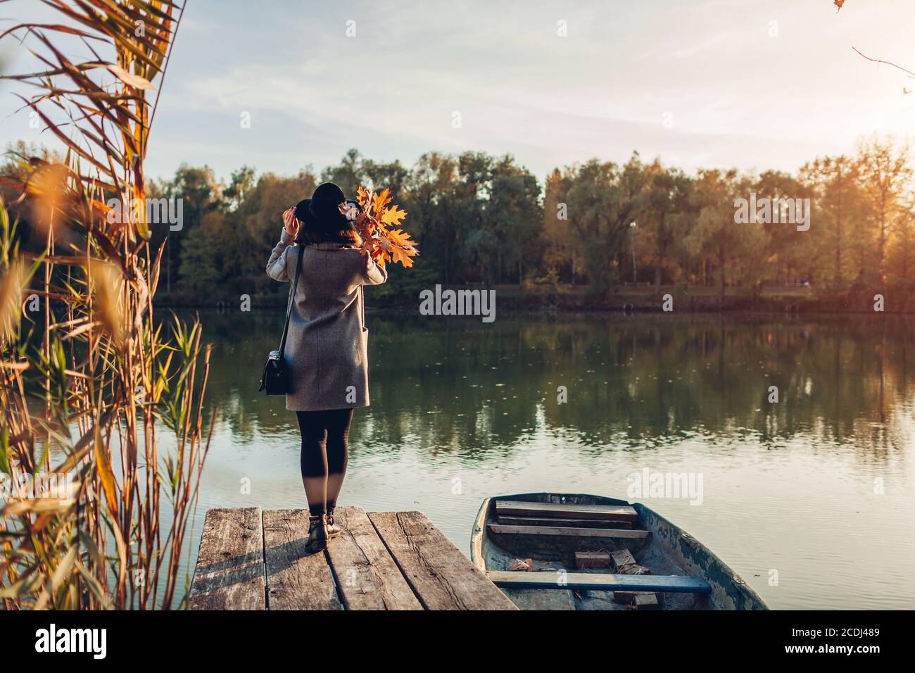 Donna che cammina sul molo del lago in barca ammirando il paesaggio autunnale che tiene le foglie. Attività della stagione autunnale Foto Stock