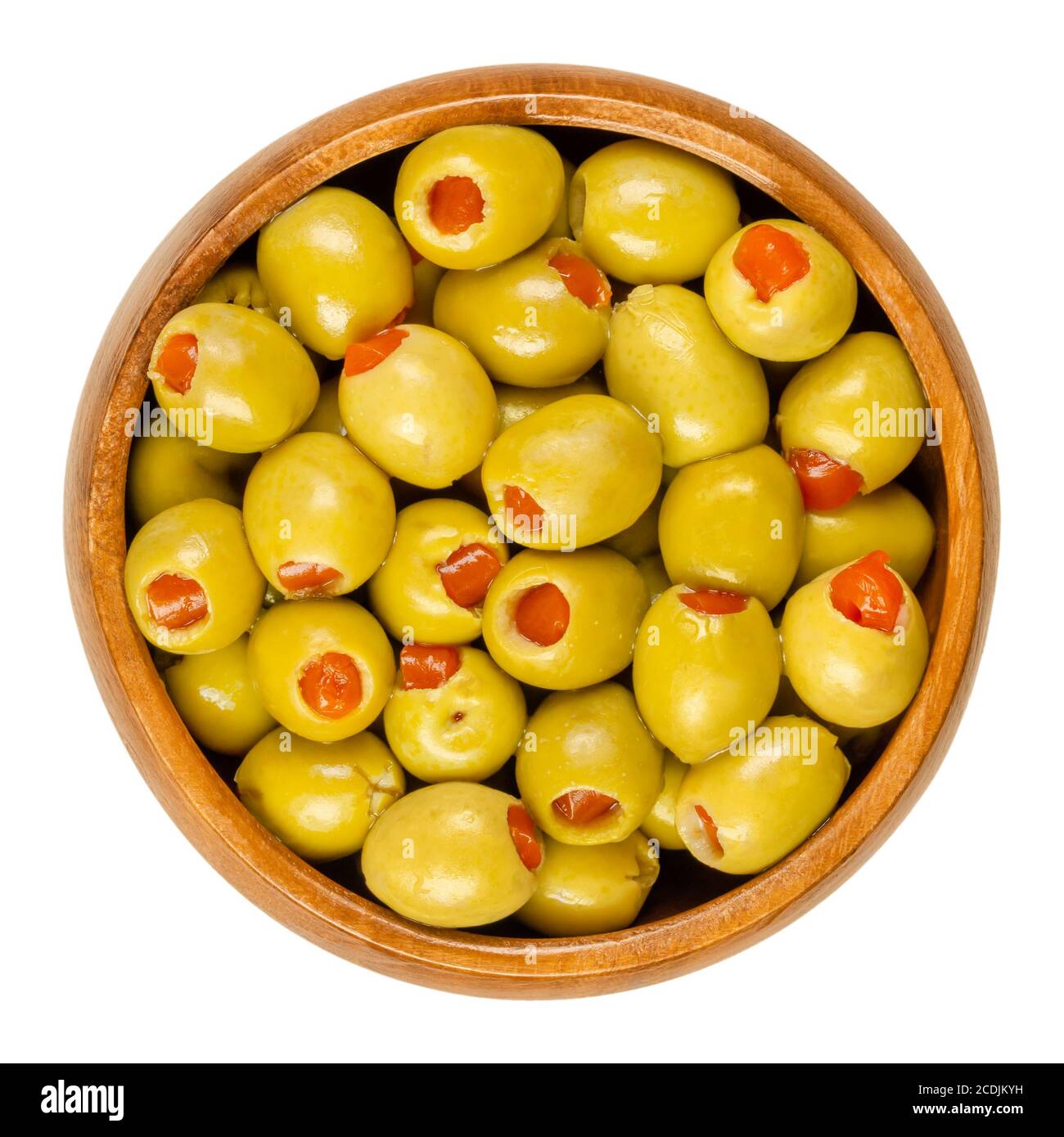 Piccole olive verdi sottaceto, farcite con peperoncino rosso in una ciotola di legno. Frutta di Olea europaea, farcita con fette di peperone. Primo piano. Foto Stock