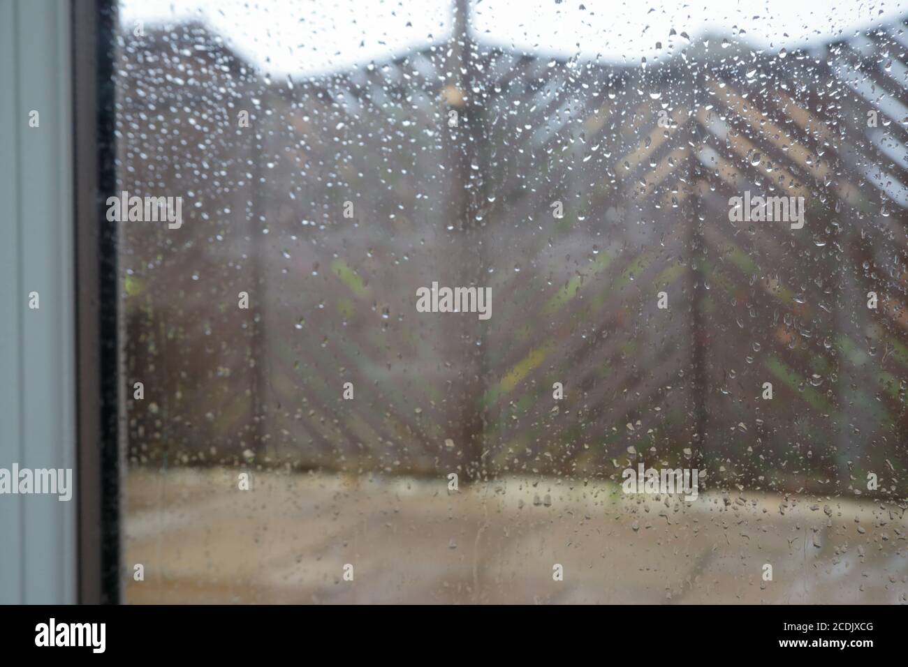 Una vista che guarda attraverso una finestra a doppi vetri spruzzata dalla pioggia che mostra un patio e recinzione in legno del giardino. Foto Stock