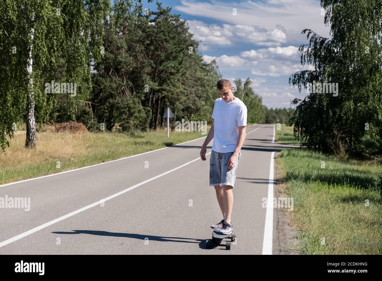 Skateboard uomo giovane adulto su asfalto contro foresta e blu cielo Foto Stock