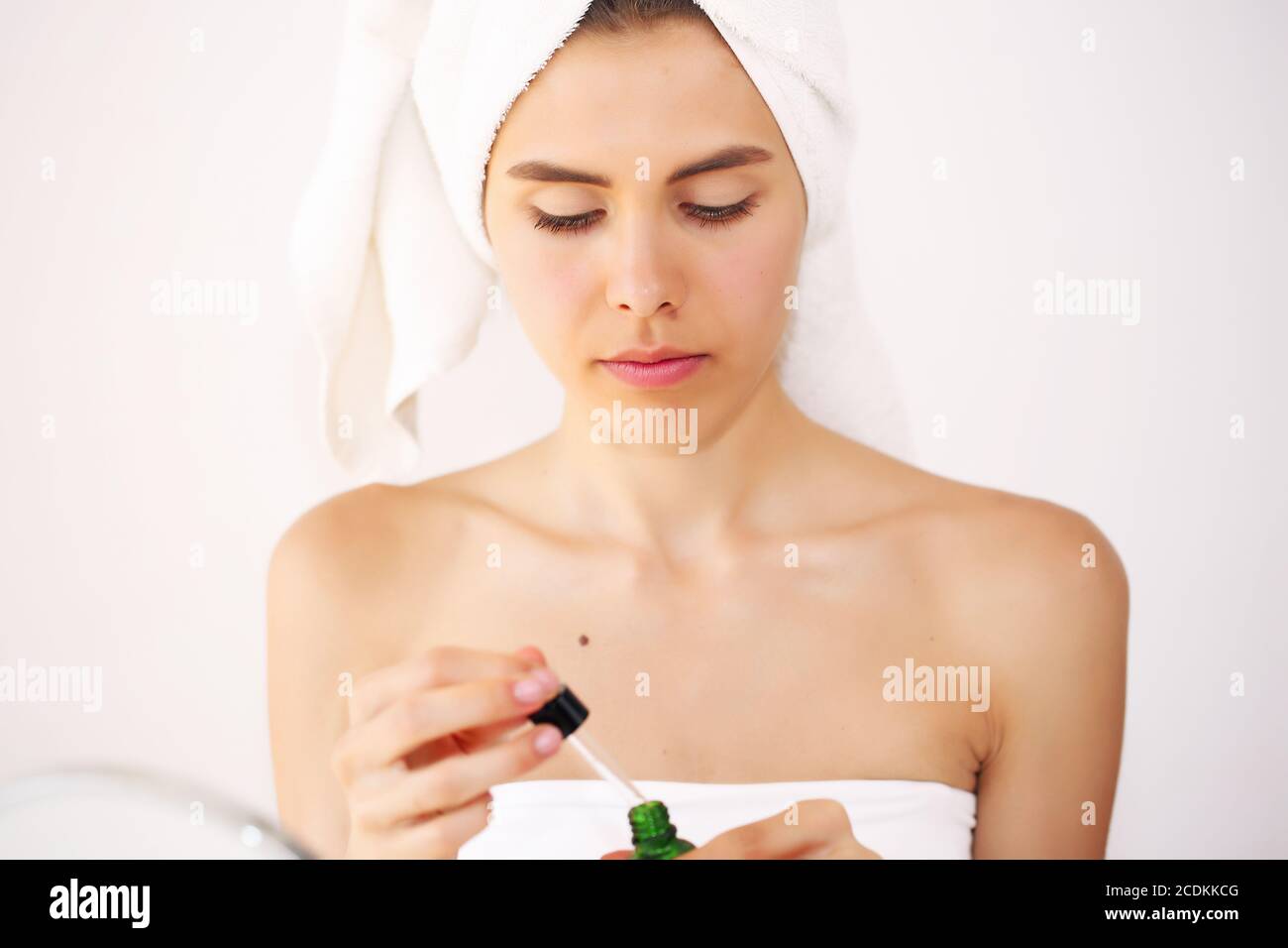 La giovane bruna si prende cura della sua pelle, in piedi davanti ad uno specchio, godendo di trattamenti di bellezza per se stessa, sorridendo teneramente Foto Stock