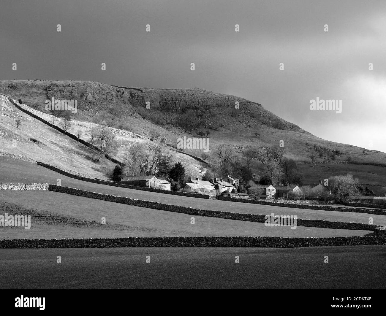 Vista in bianco e nero degli edifici in pietra del villaggio di Feizor tra i campi, muri a secco in pietra e cicatrice calcarea nei pressi di Austwick, North Yorkshire, Inghilterra, Regno Unito Foto Stock