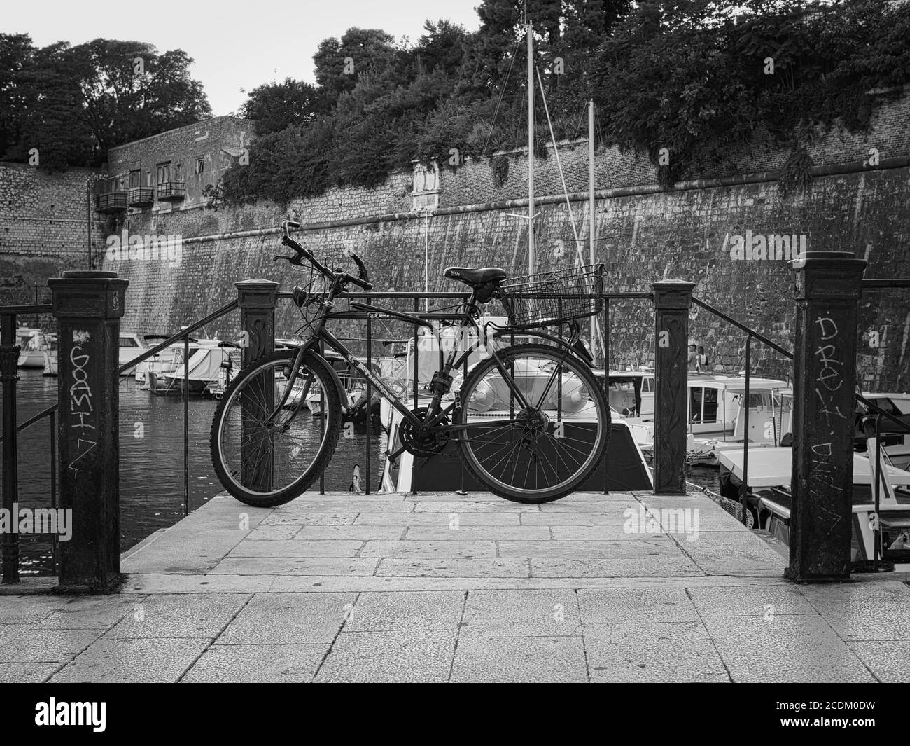 Una bicicletta tra le scale nel centro della città di Zara, Croazia, Europa. Fotografato in bianco e nero. Sullo sfondo si vedono alcune barche. Foto Stock