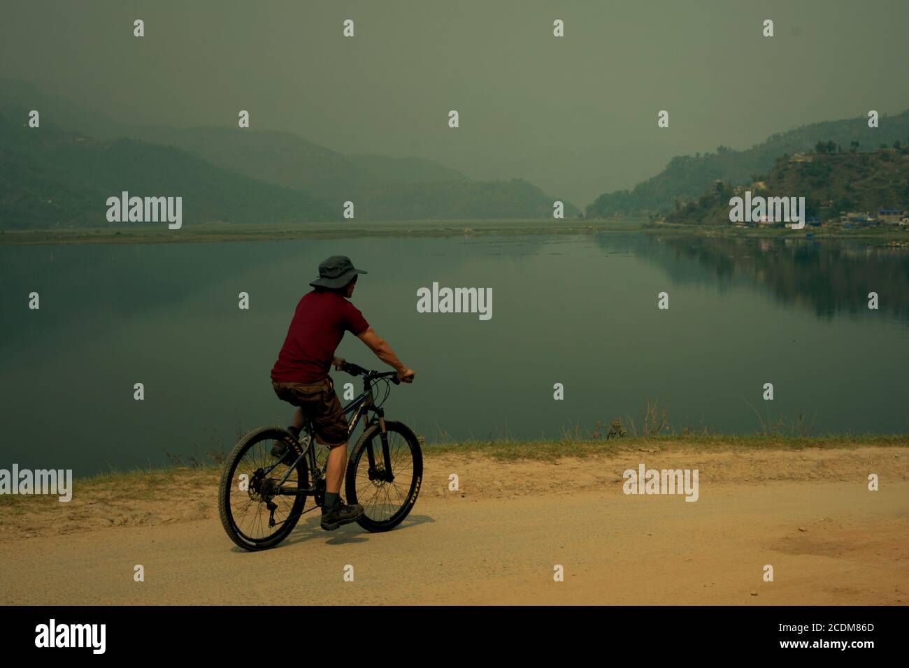 Un ciclista che si muove sulla strada rurale sul lato del lago di Phewa a Pokhara, Gandaki Pradesh, Nepal. Foto Stock