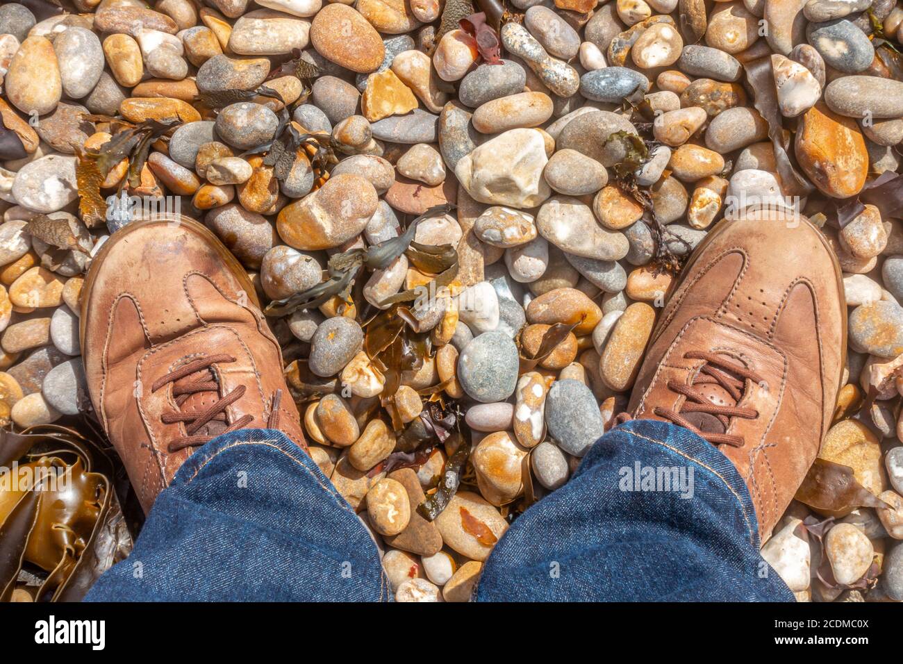 Un paio di piedi maschi in pelle marrone fa su una spiaggia di ciottoli. Foto Stock