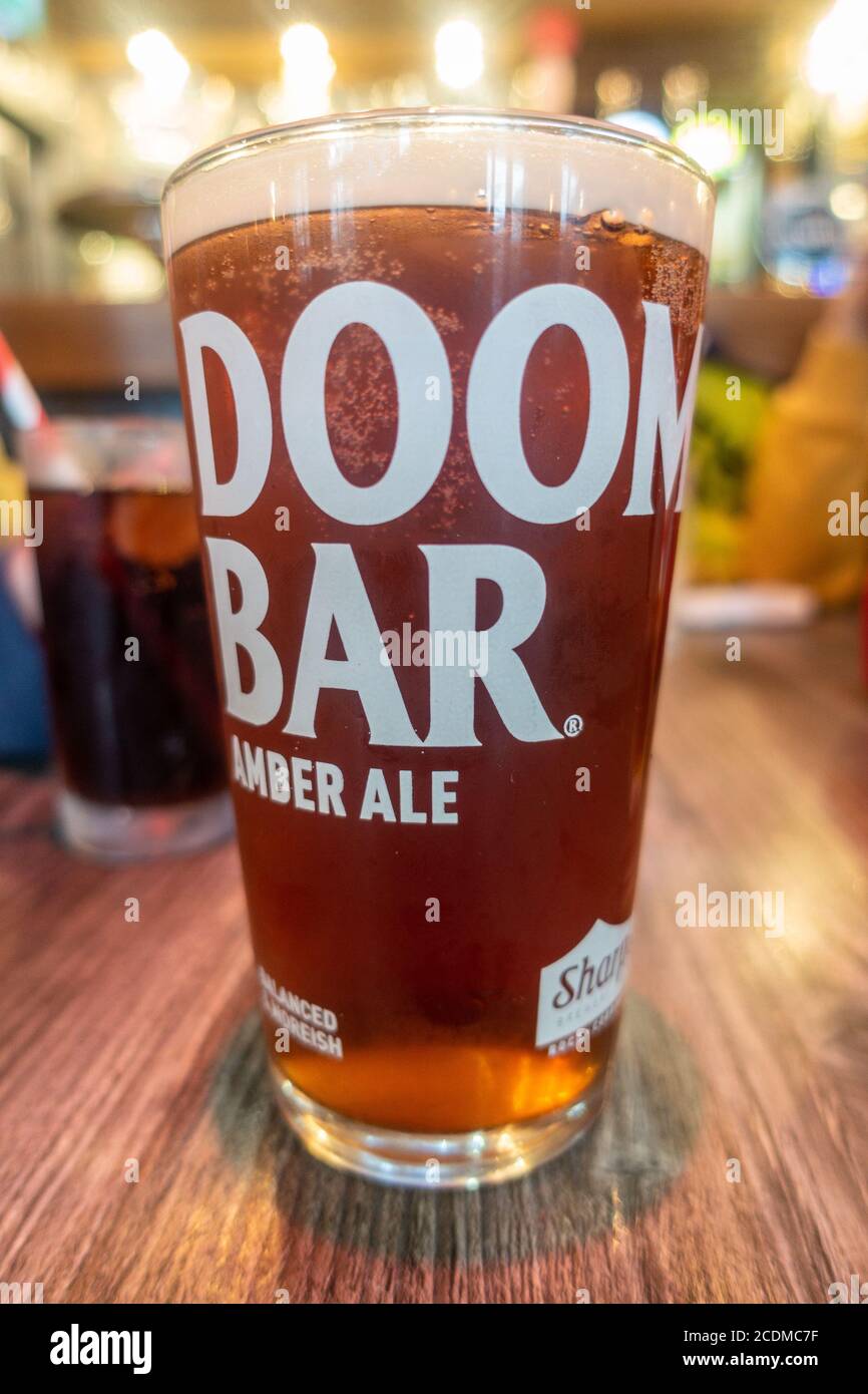 Una pinta di Doom Bar Amber Ale in una pinta di vetro su un tavolo di legno in un pub. Foto Stock