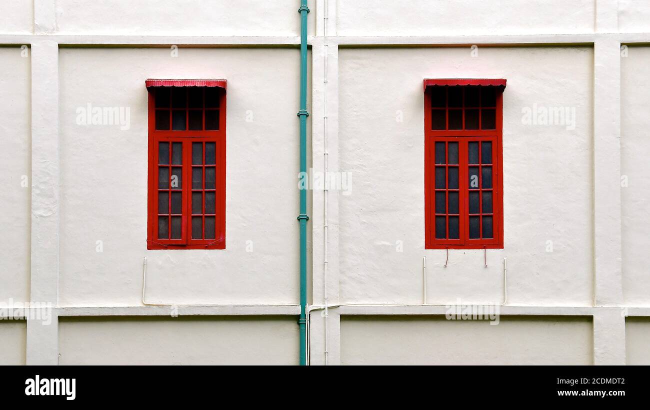 Una vista ravvicinata di due finestre rosse in un vecchio edificio coloniale restaurato con pareti in pietra bianca. Foto Stock