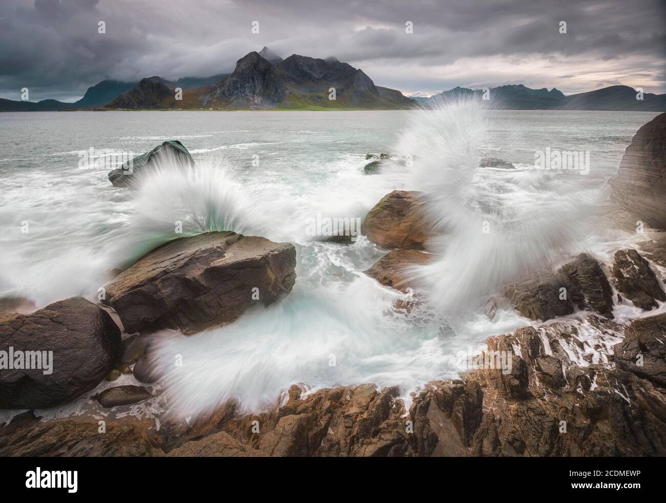 Onde splashing su costa rocciosa, dietro le montagne di Lofoten, Lofoten, Nordland Foto Stock