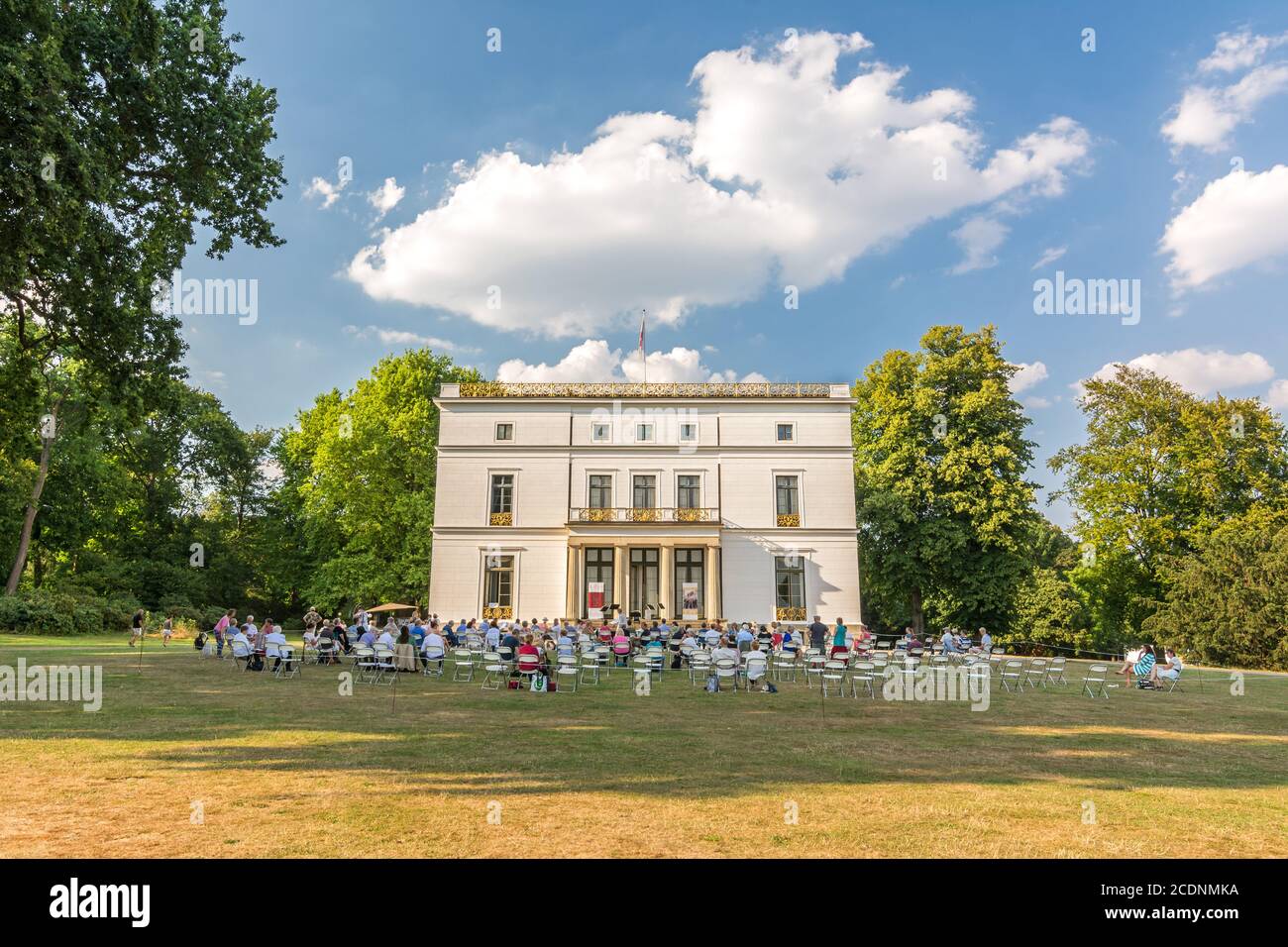 Pubblico di un concerto all'aperto in un parco (Jenischpark ad Amburgo, Germania) di fronte a una bella residenza bianca in estate Foto Stock