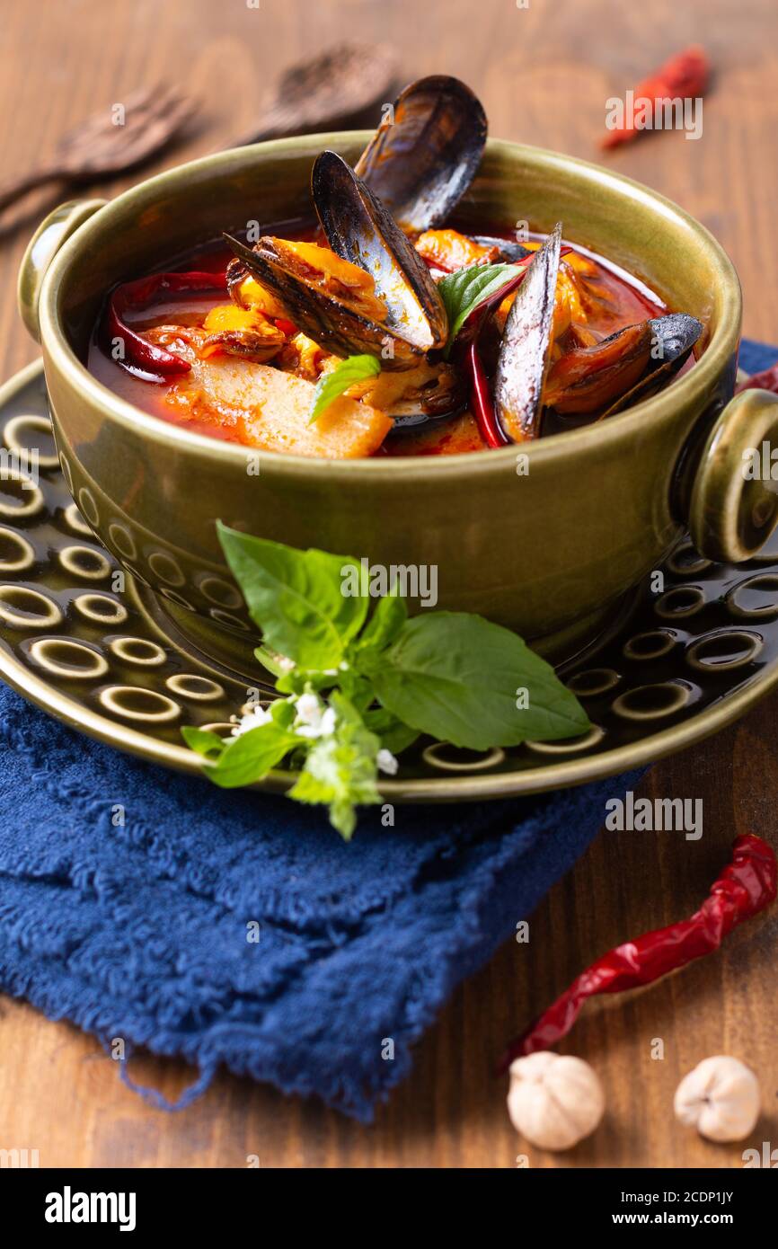 Concetto di cibo Tailandese amareggiato di curry rosso cozze ananas Kang Kua Hoi in recipiente di ceramica verde su fondo di legno di tovagliolo blu con spazio per la copia Foto Stock