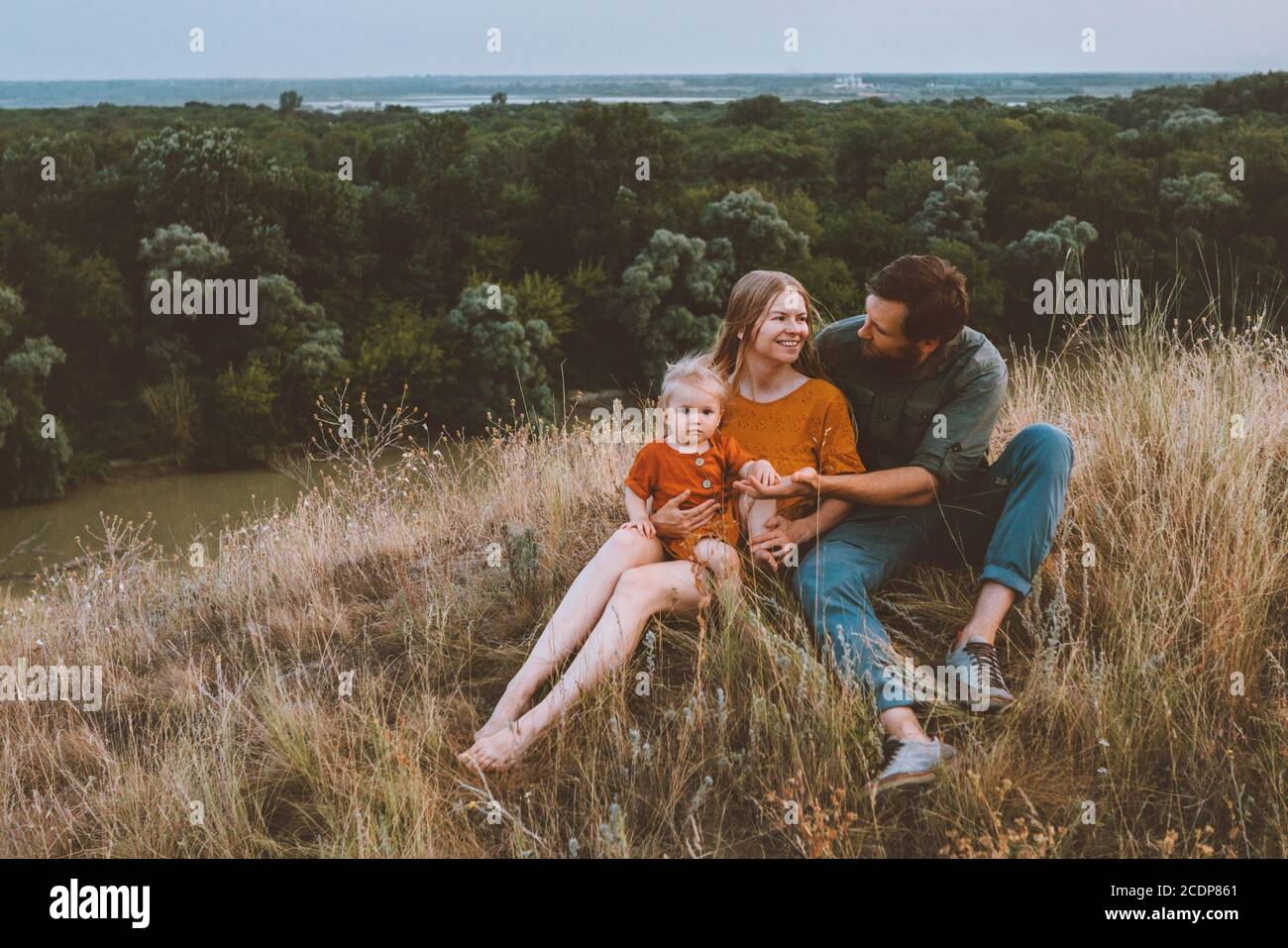 Famiglia genitori con bambino che si diverte madre e padre all'aperto con il bambino seduto su erba sano stile di vita staycation fine settimana rurale natura Foto Stock