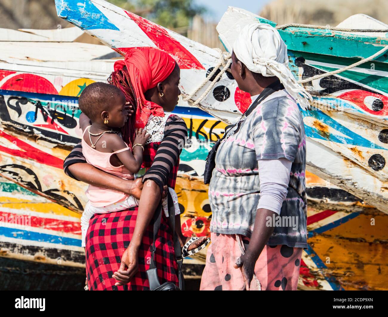 Nianing, Senegal - 24 gennaio 2019: Donna senegalese e la chiocciera sullo sfondo di colorate barche da pesca in legno in piedi sulla spiaggia di sabbia in Senegal. Foto Stock