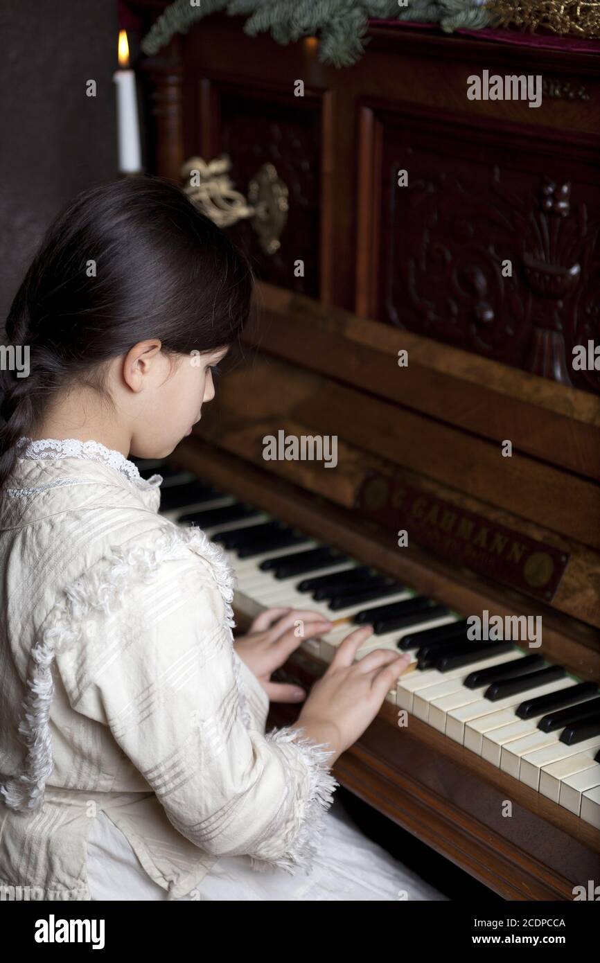 La ragazza giovane in un vestito storico sta giocando su un pianoforte antico Foto Stock