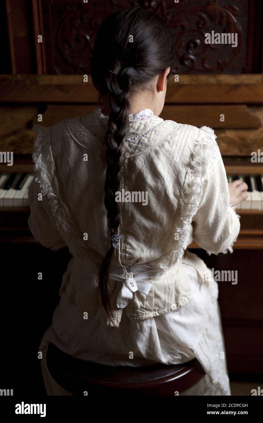 La ragazza giovane in un vestito storico sta giocando su un pianoforte antico Foto Stock