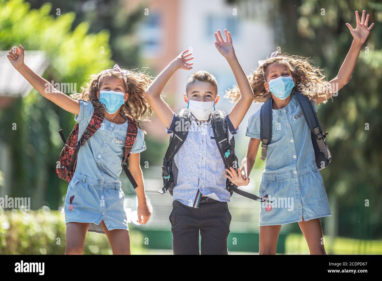 Studenti felici con maschere facciali saltano dalla gioia per tornare a scuola durante la quarantena Covid-19. Foto Stock