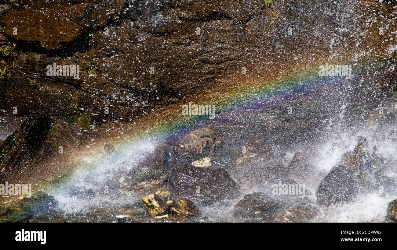 Un bell'arcobaleno si forma sotto una cascata a causa della luce solare che passa attraverso le goccioline d'acqua in una giornata di sole. Foto Stock