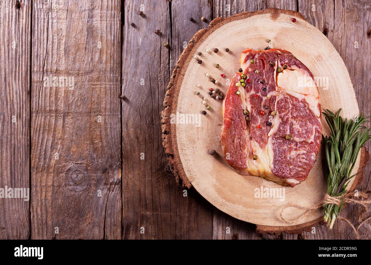 Bistecca di manzo con rosmarino e pepe su sfondo di legno, vista dall'alto Foto Stock