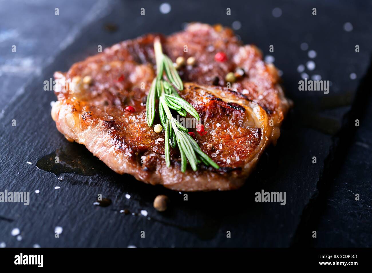 Bistecca di manzo su un piatto scuro con rosmarino e pepe, fuoco selettivo Foto Stock