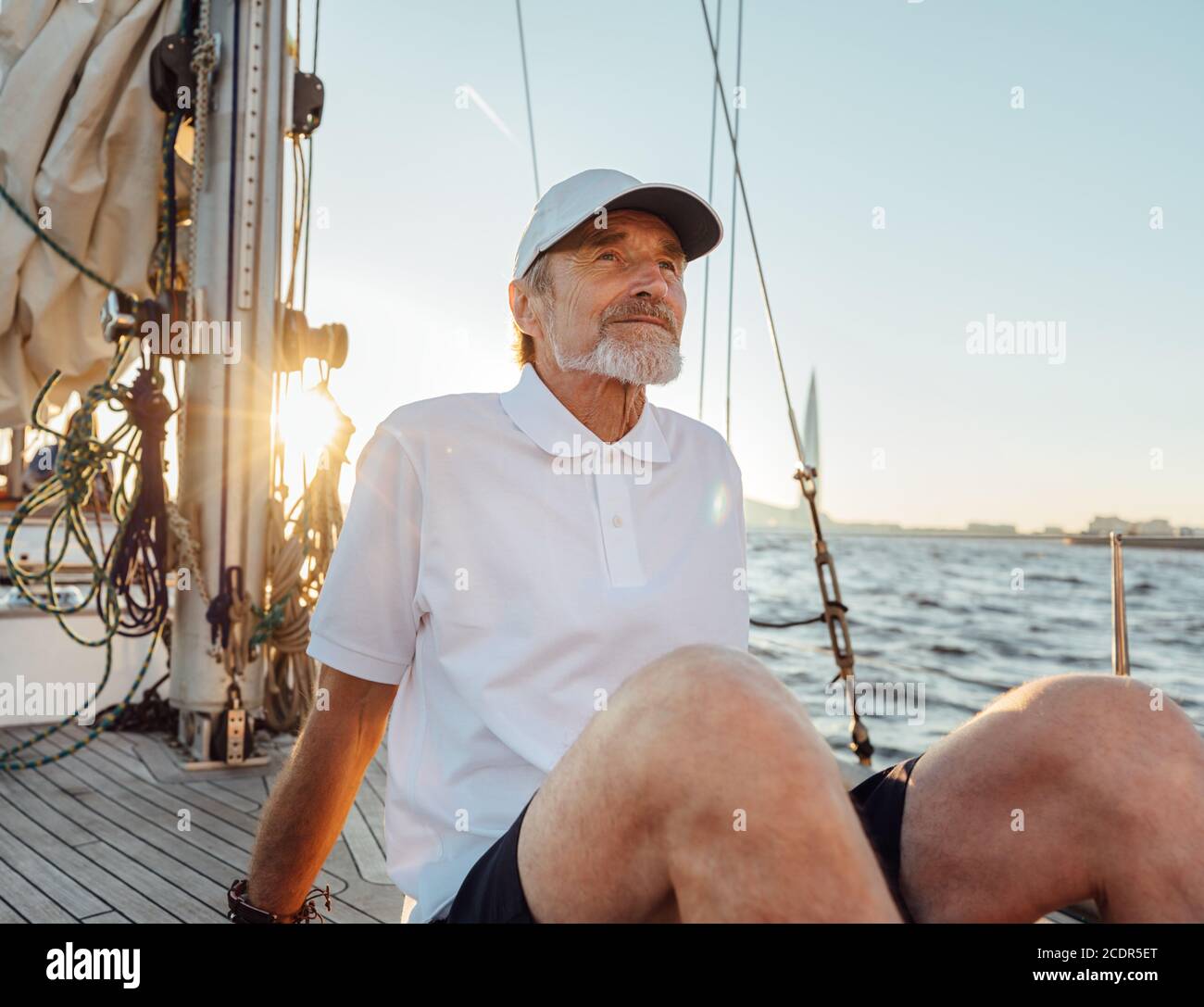 Ritratto di un uomo maturo seduto sul suo yacht. Capitano senior che gode di un tramonto su una barca a vela. Foto Stock