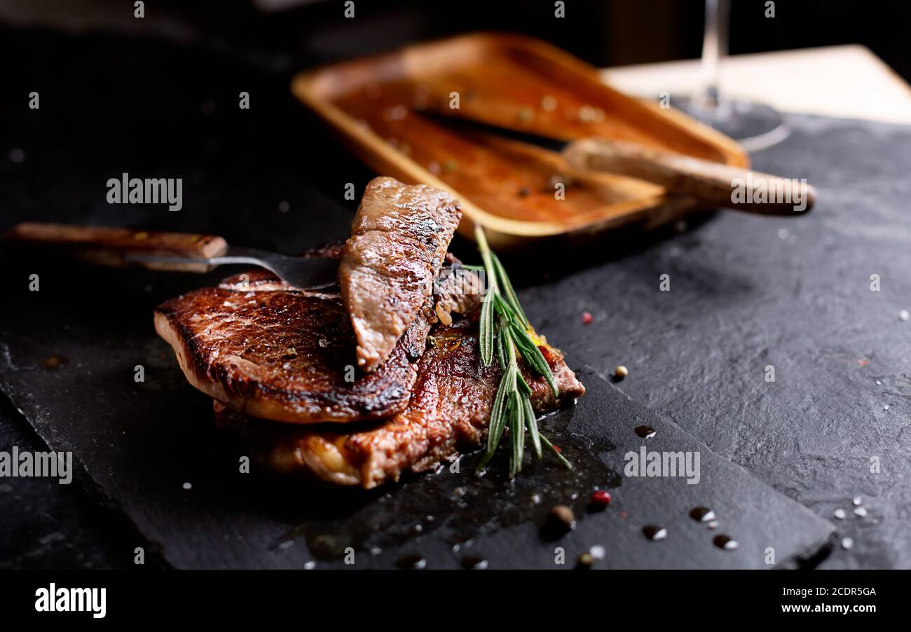 Pezzi di bistecca di manzo su un piatto scuro con rosmarino e pepe, fuoco selettivo Foto Stock
