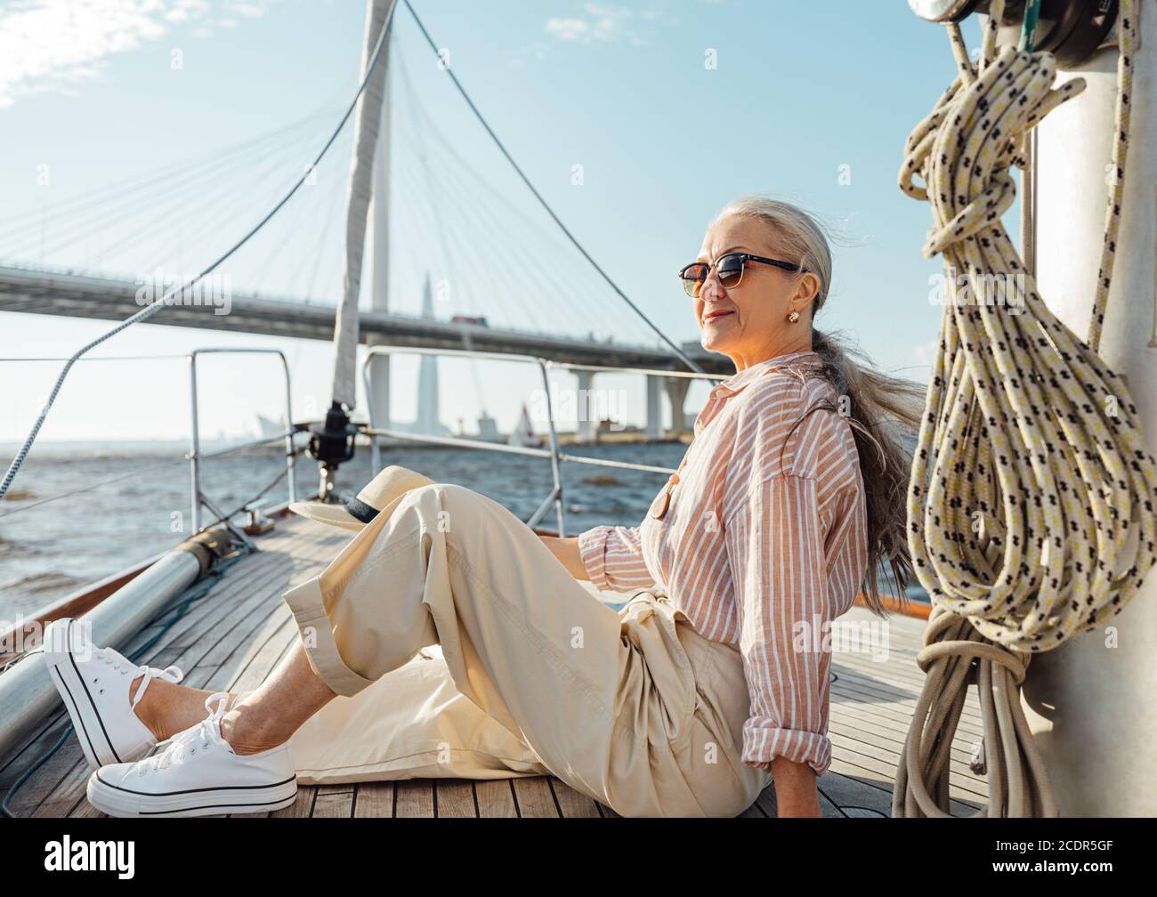 Donna matura ed elegante seduta su un arco di yacht. Donna anziana che si gode la vacanza su una barca a vela privata. Foto Stock