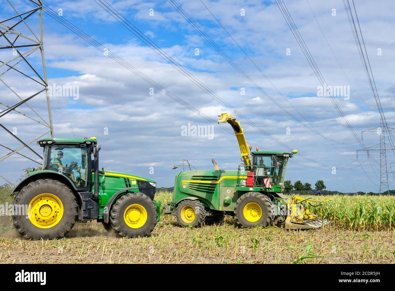 Germania agricoltura che raccoglie mais sotto linee ad alta tensione e piloni Trattore John Deere Foto Stock