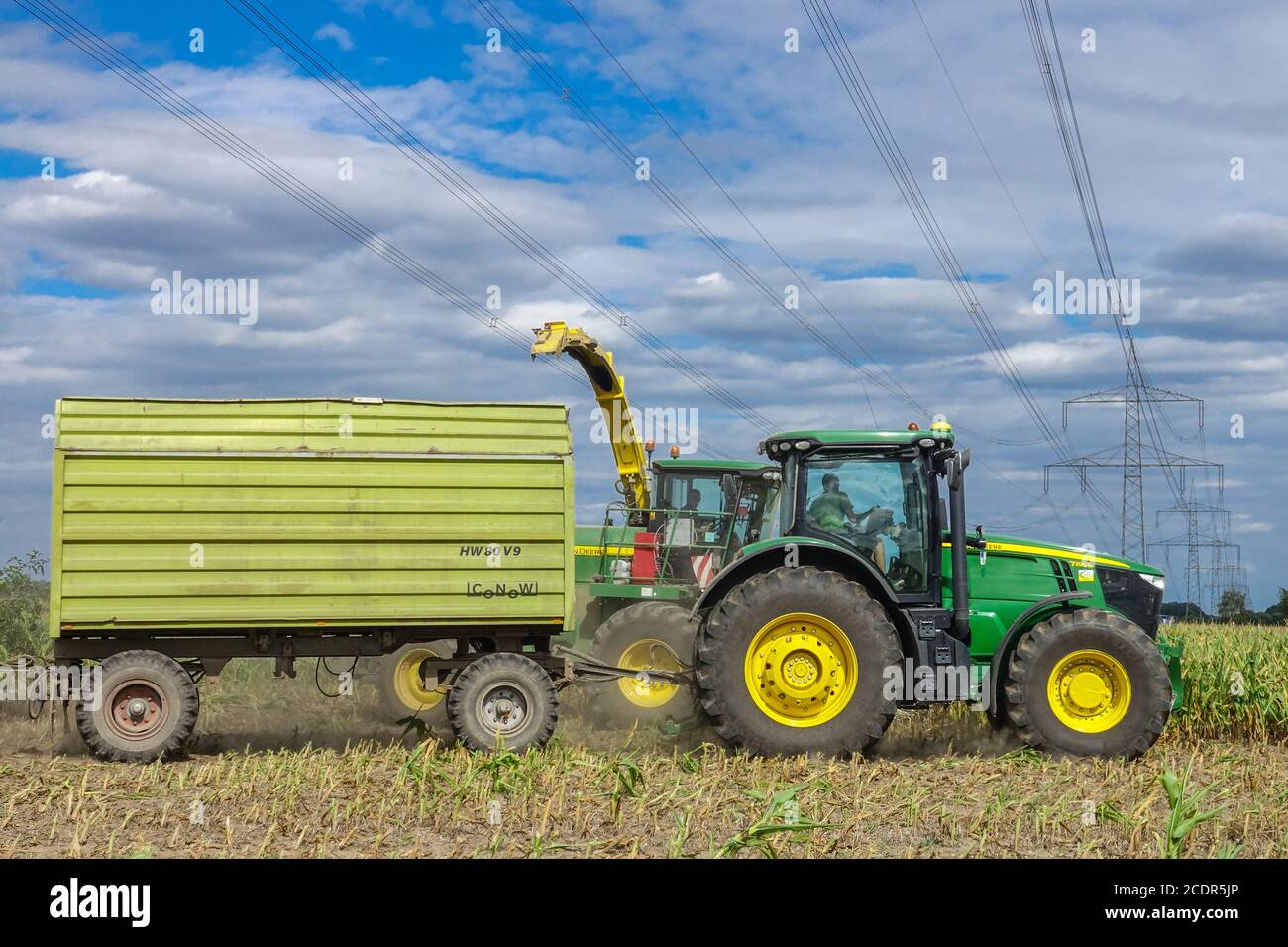 Agricoltura che raccoglie mais sotto linee ad alta tensione e piloni John Trattore Deere Foto Stock