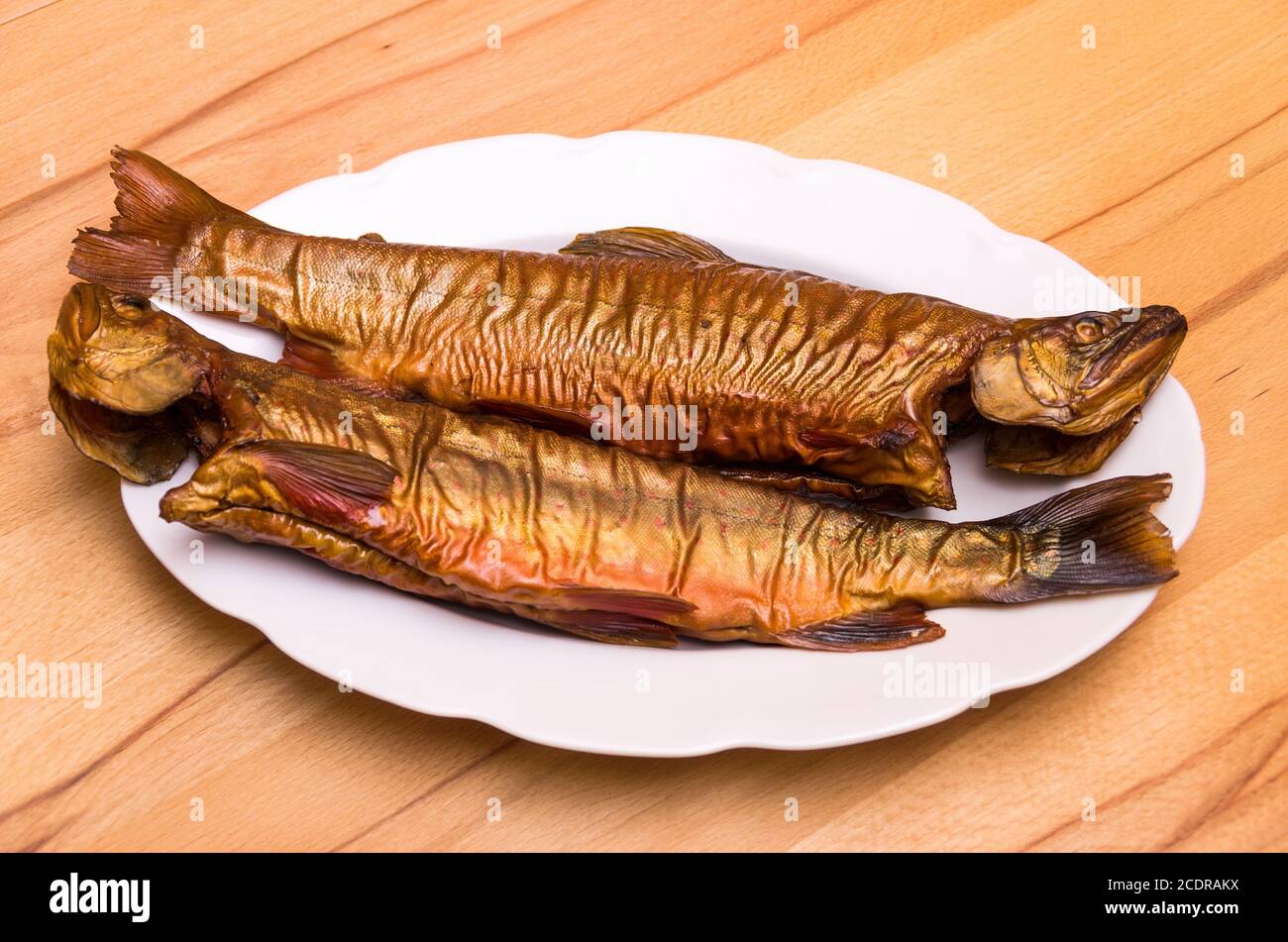 Due pesci affumicati, trota di ruscello, su un piatto bianco su un tavolo di faggio. Foto Stock