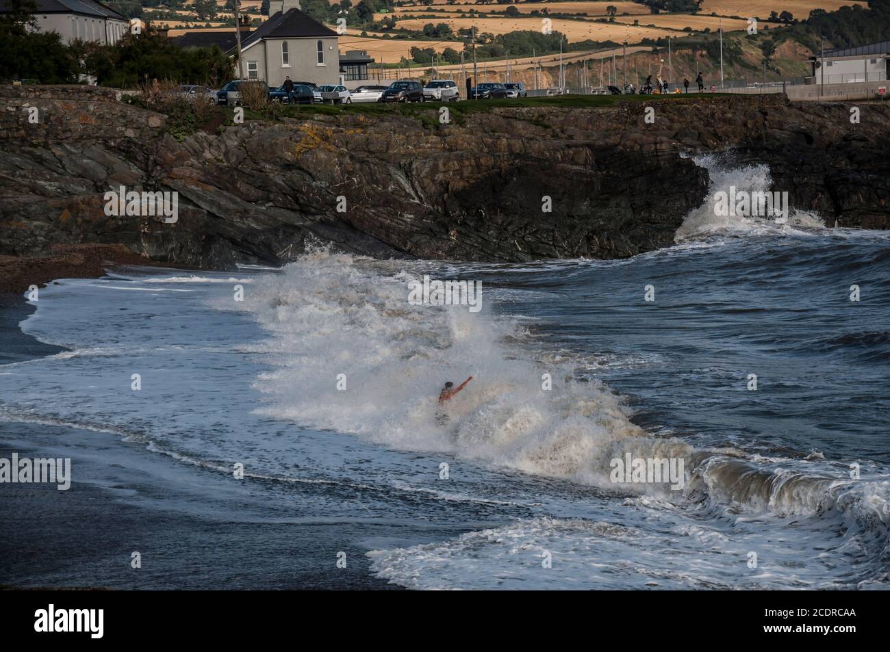 Visitare Greystones. L'uomo di mezza età rimane davanti all'onda di rottura godendosi il relativo spruzzi. Foto Stock