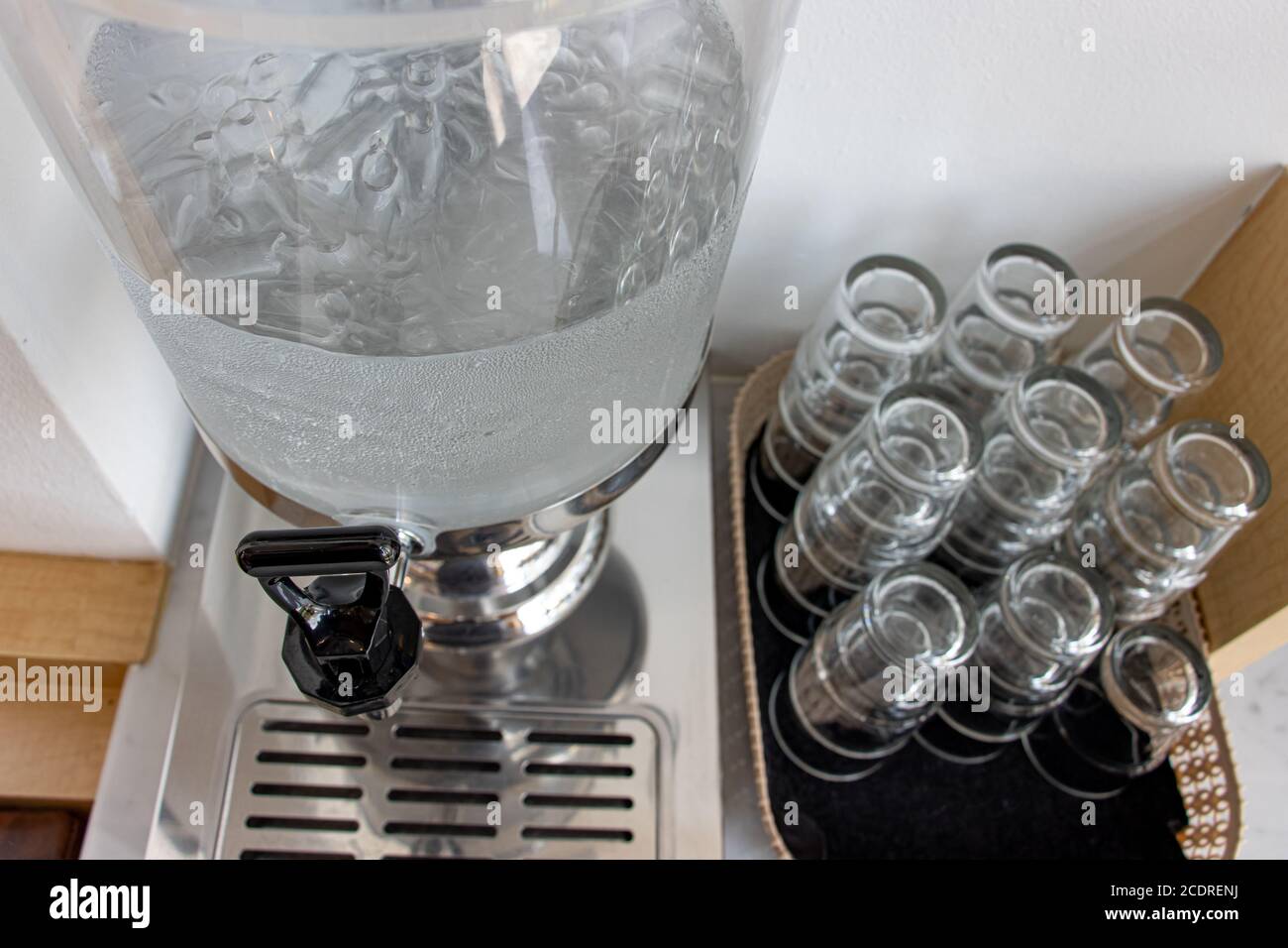 Pulire l'acqua potabile con ghiaccio in un dispenser self-service con vetro sul tavolo. Rubinetto da contenitore di vetro per acqua fredda al buffet self service Foto Stock