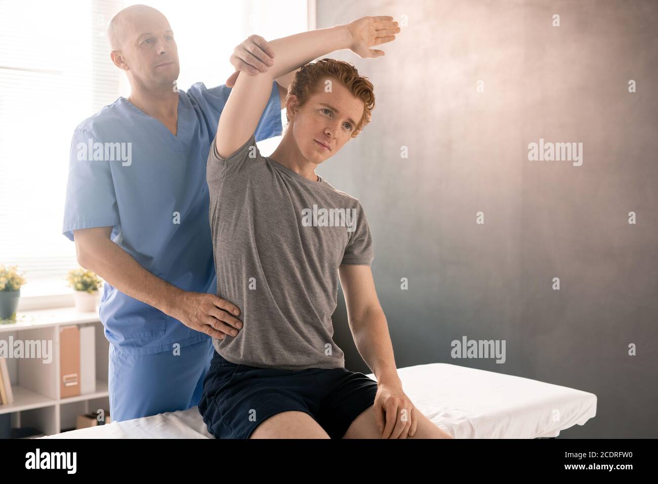 Fisioterapista maturo in braccio di supporto uniforme del paziente durante le curvature laterali Foto Stock