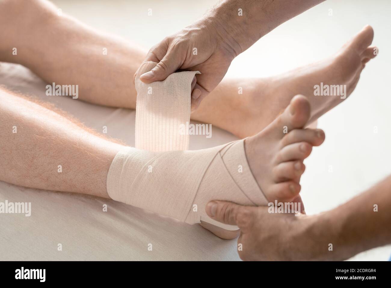 Mani di medico di riabilitazione che avvolge il piede e la caviglia dell'uomo con bendaggio Foto Stock