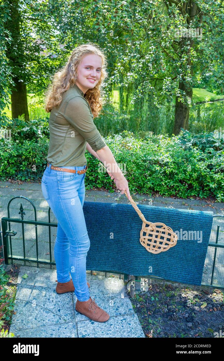 Giovane donna olandese che batte il tappetino della portiera con battitoio per tappeti Foto Stock