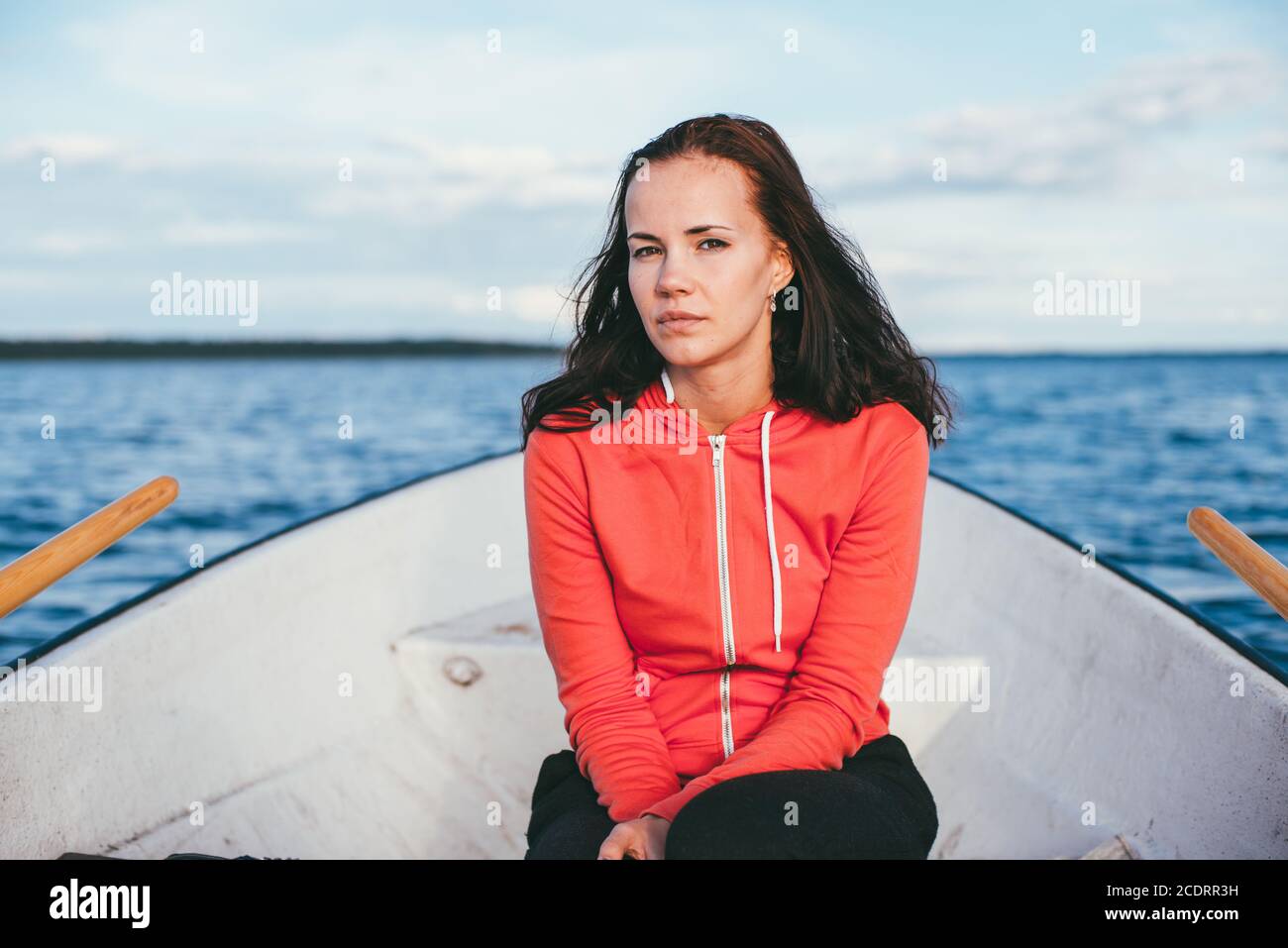 Incredibile bella ragazza dai capelli nuota su una barca di legno e canottaggio con remi in uno splendido lago di primavera. Stile di vita senza trucco Foto Stock
