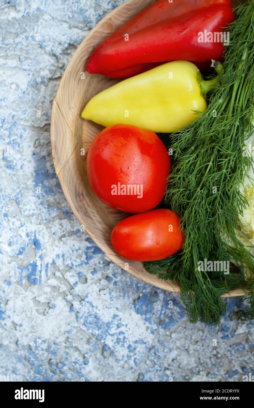 Pomodori rossi, peperoni giallo-verdi e rossi, aneto, cavolo giacciono su un piatto di legno su sfondo blu. Vista dall'alto. Spazio di copia Foto Stock