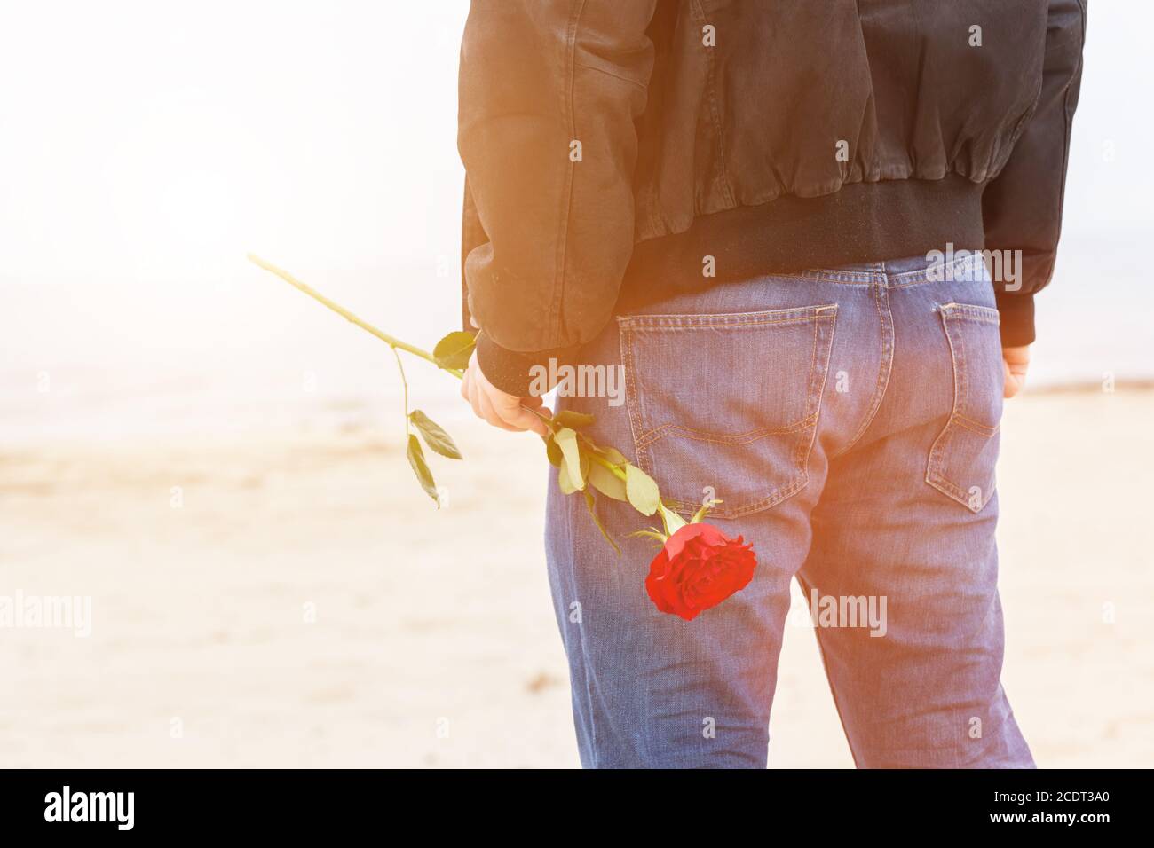 Uomo con una rosa dietro la schiena in attesa di amore. Data romantica sulla spiaggia Foto Stock