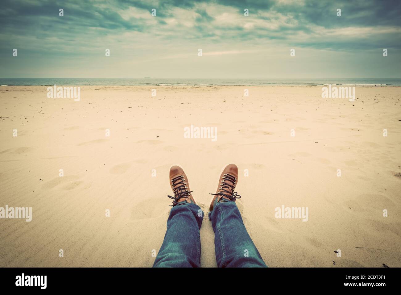 Prospettiva in prima persona delle gambe dell'uomo in jeans sul spiaggia d'autunno Foto Stock