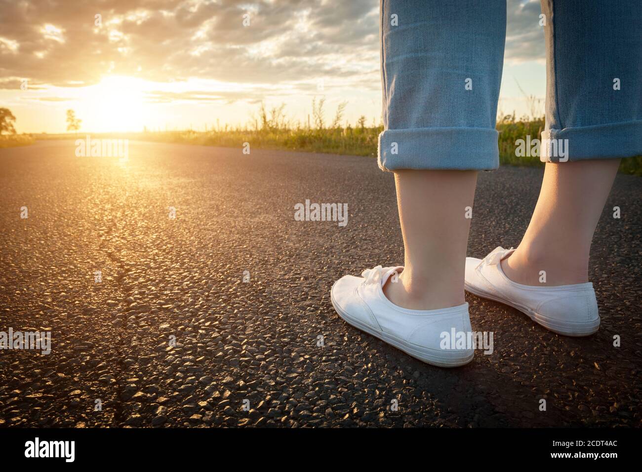 Donna in sneakers bianche in piedi su strada asfaltata verso il sole. Concetti di viaggio, libertà. Foto Stock