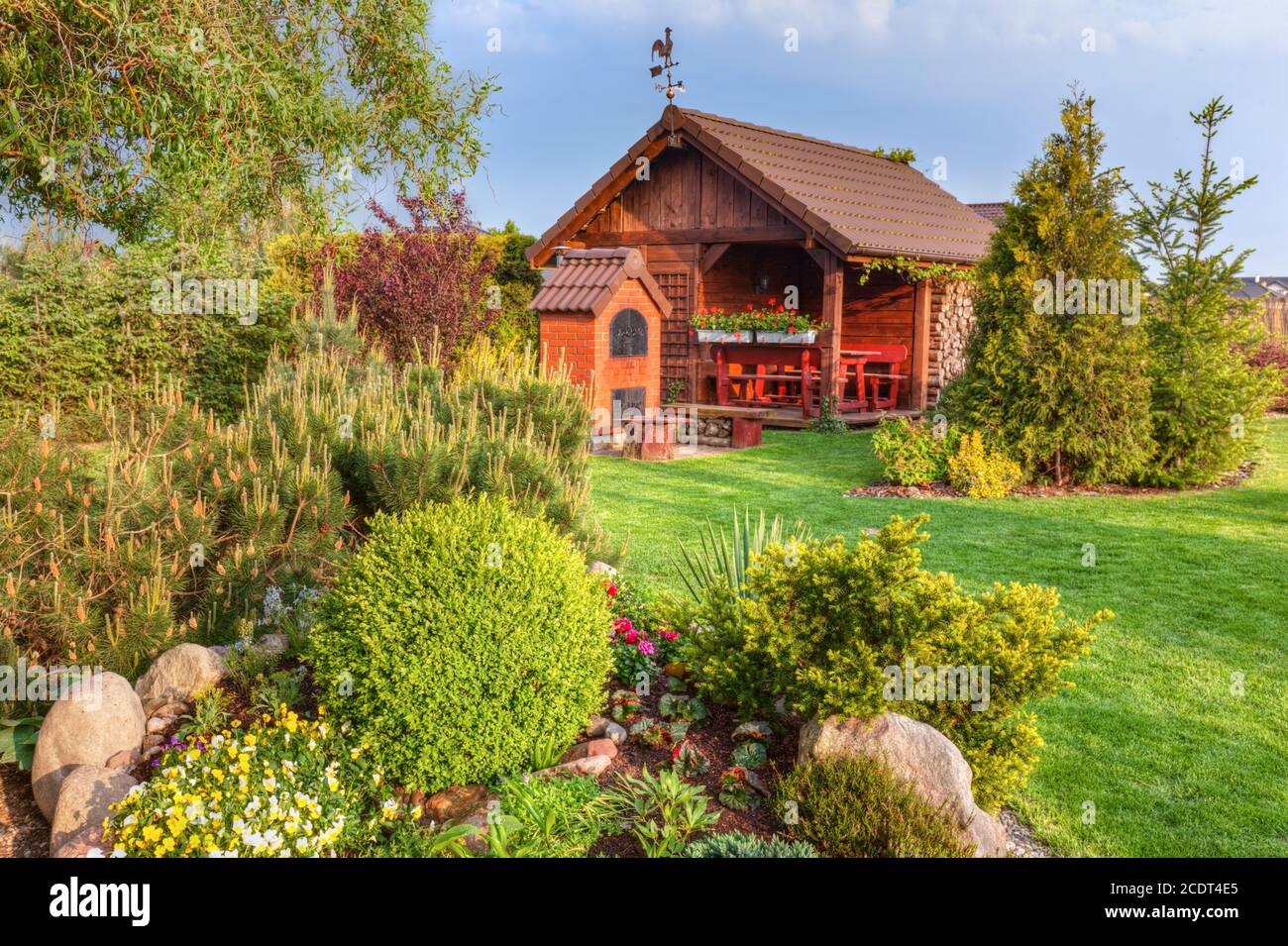 Giardino estivo paesaggistico con barbecue e casa estiva in legno alberi verdi, aiuole, Foto Stock