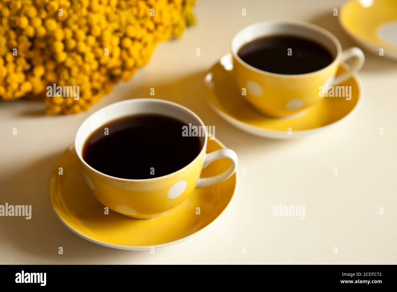Due tazze di caffè gialle su sfondo bianco, pausa caffè e aggiunta di caffeina concetto. Fiori gialli sul tavolo Foto Stock