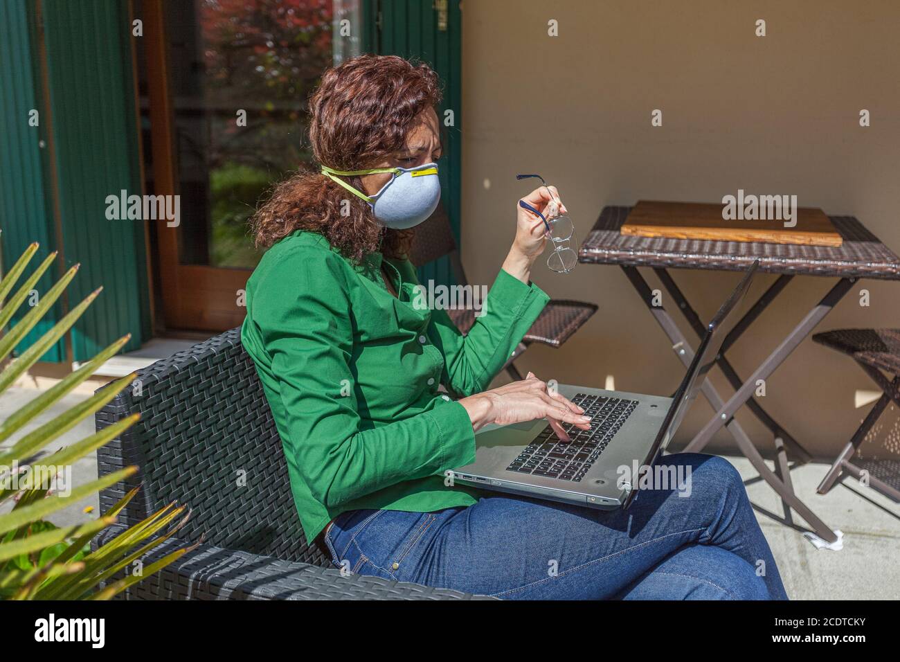 Donna seduta in un giardino con maschera antivirus che guarda computer portatile Foto Stock