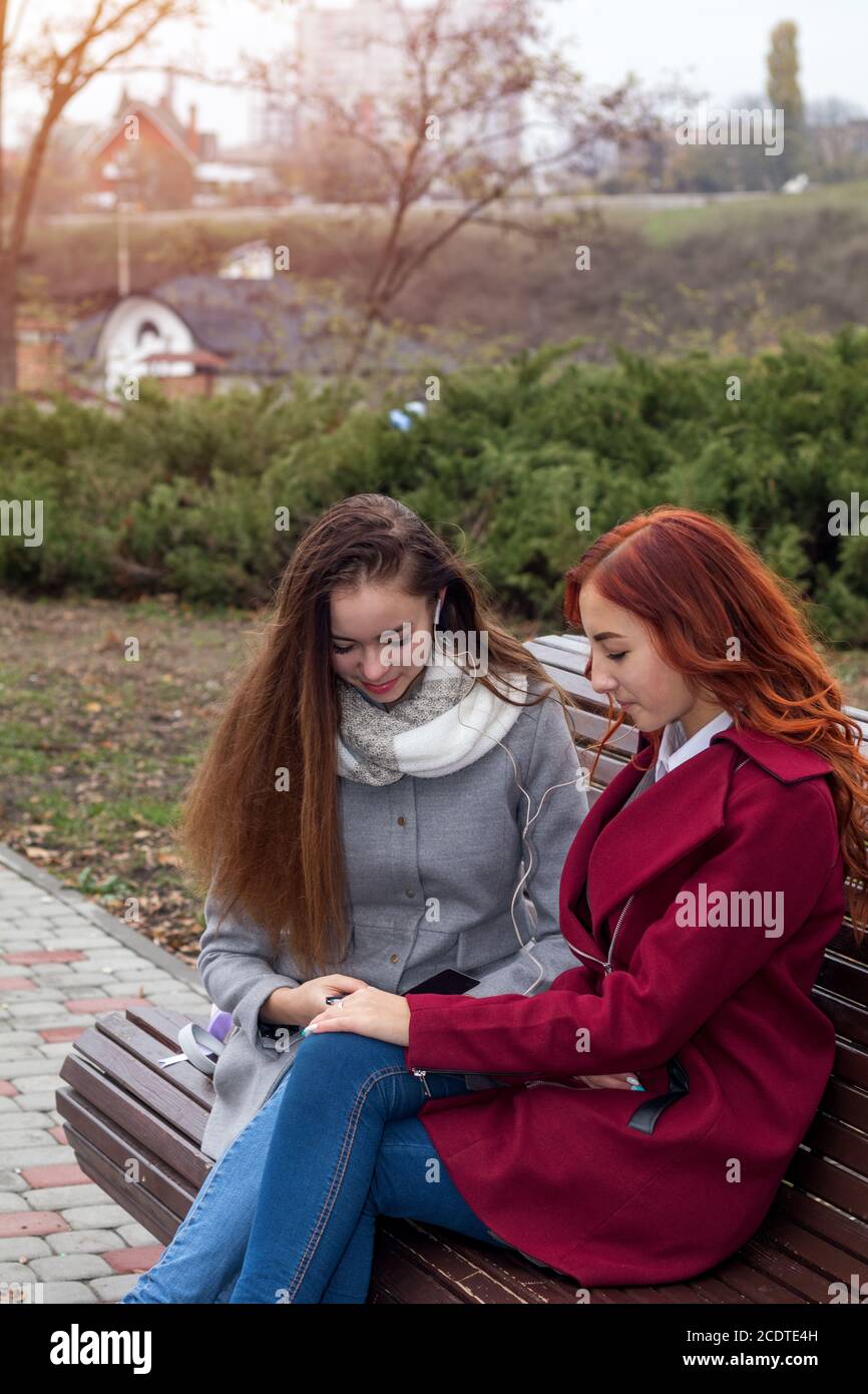 Gli adolescenti di sesso femminile a discutere di un libro seduti sul banco in un autunno city park Foto Stock