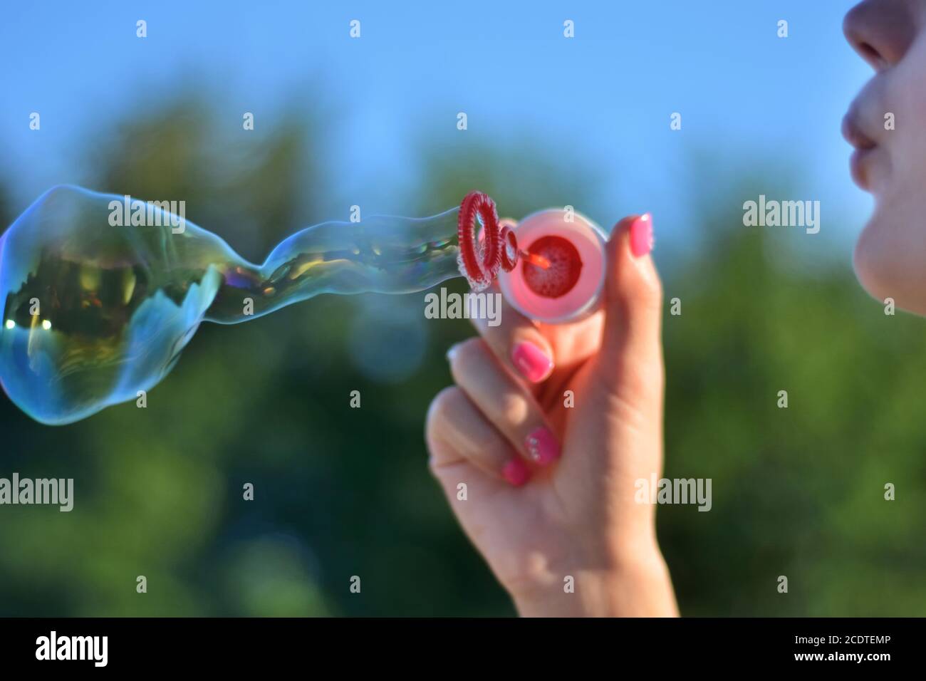 Ragazza che soffia bolle di sapone all'aperto nel parco al tramonto estivo. Felicità in natura concetto. Primo piano, messa a fuoco selettiva Foto Stock