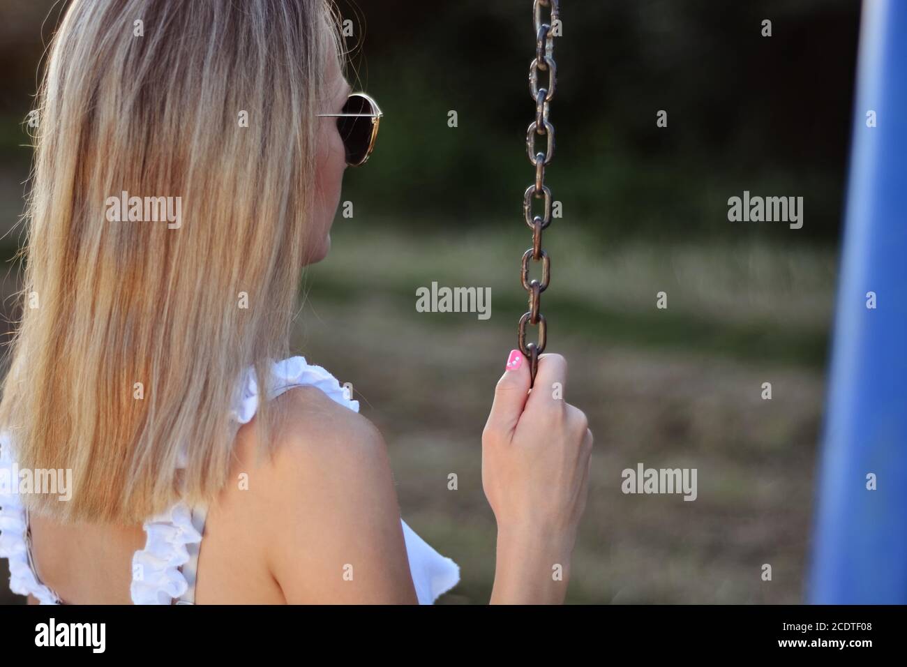 Donna seduta su un'altalena e tiene la mano alla catena metallica nel parco in una giornata estiva soleggiata. Relax nel concetto di parco Foto Stock