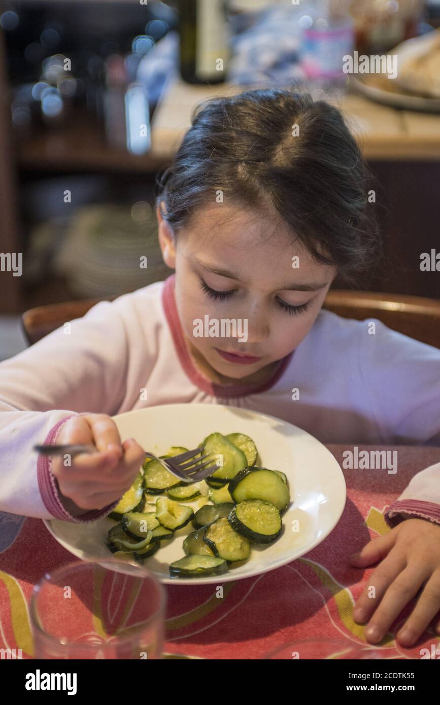la bambina di 5 anni mangia zucchine cotte in cucina tavolo al mattino ancora in pigiama Foto Stock
